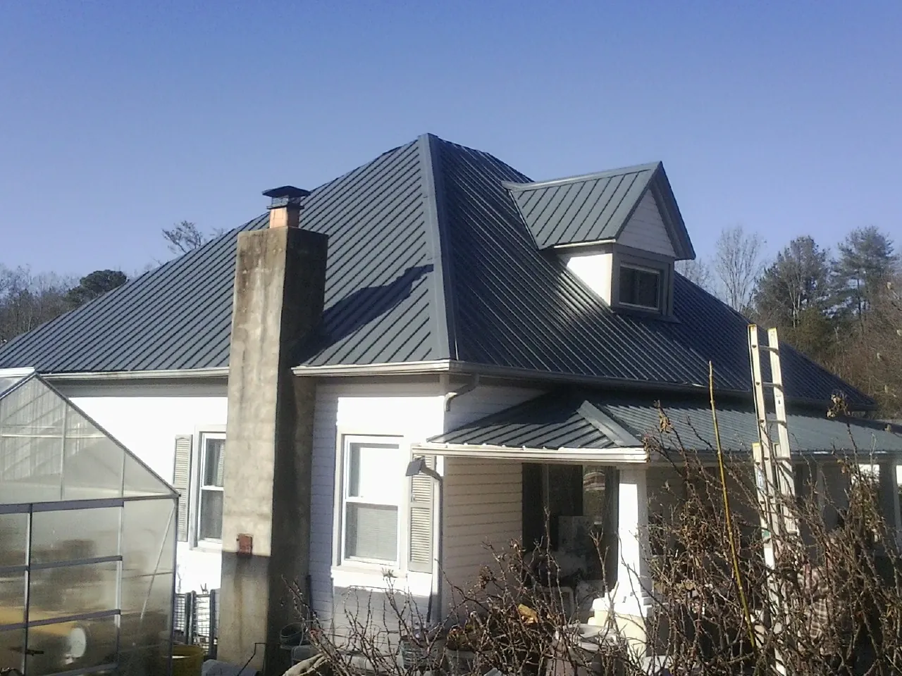 Dark blue standing seam metal roof on a white farmhouse with dormer — Slate & Tile Roof Repair by Roofing Brothers in Marshalltown