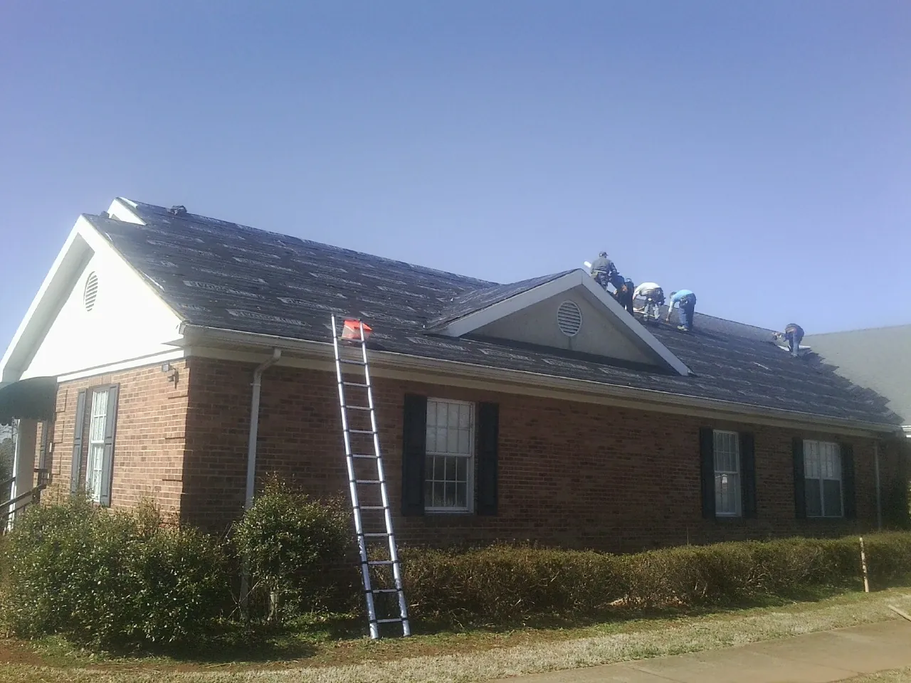 Crew tearing shingles off a brick ranch roof with a ladder set — Emergency Roof Repair work by our crew in Marshalltown