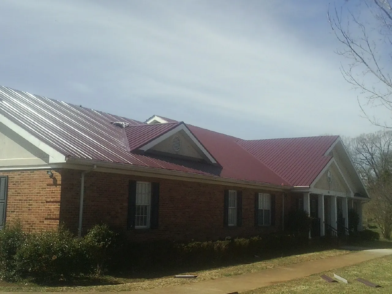 Red metal roof with gabled entries on a long brick building, from a Hail Damage Roof Repair job in Marshalltown