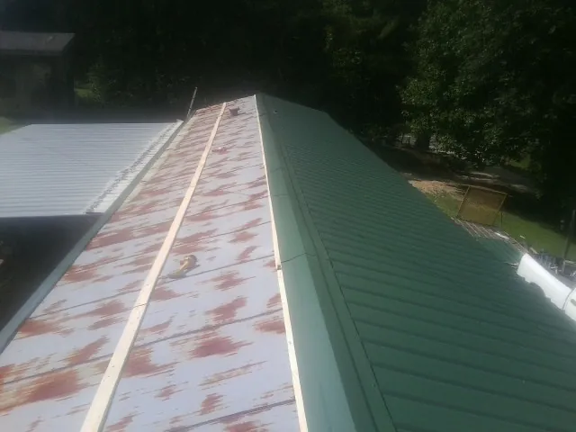 Old rusted panels beside newly installed green metal roofing — Wind Damage Roof Repair by Roofing Brothers in Marshalltown
