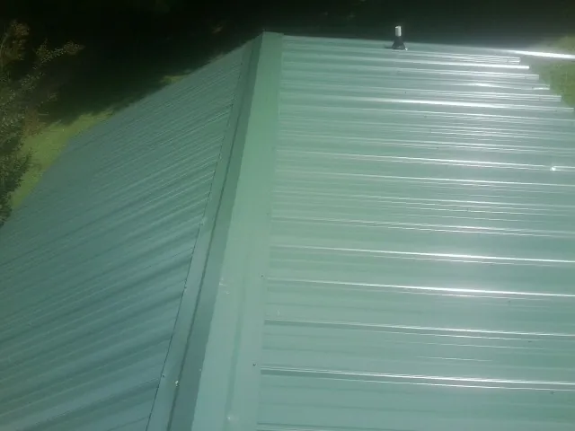 New green metal panels meeting at the ridge of a roof — Flat Roof Repair work by our crew in Marshalltown