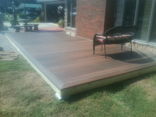 New wood deck and wicker chair beside a brick house in Marshalltown