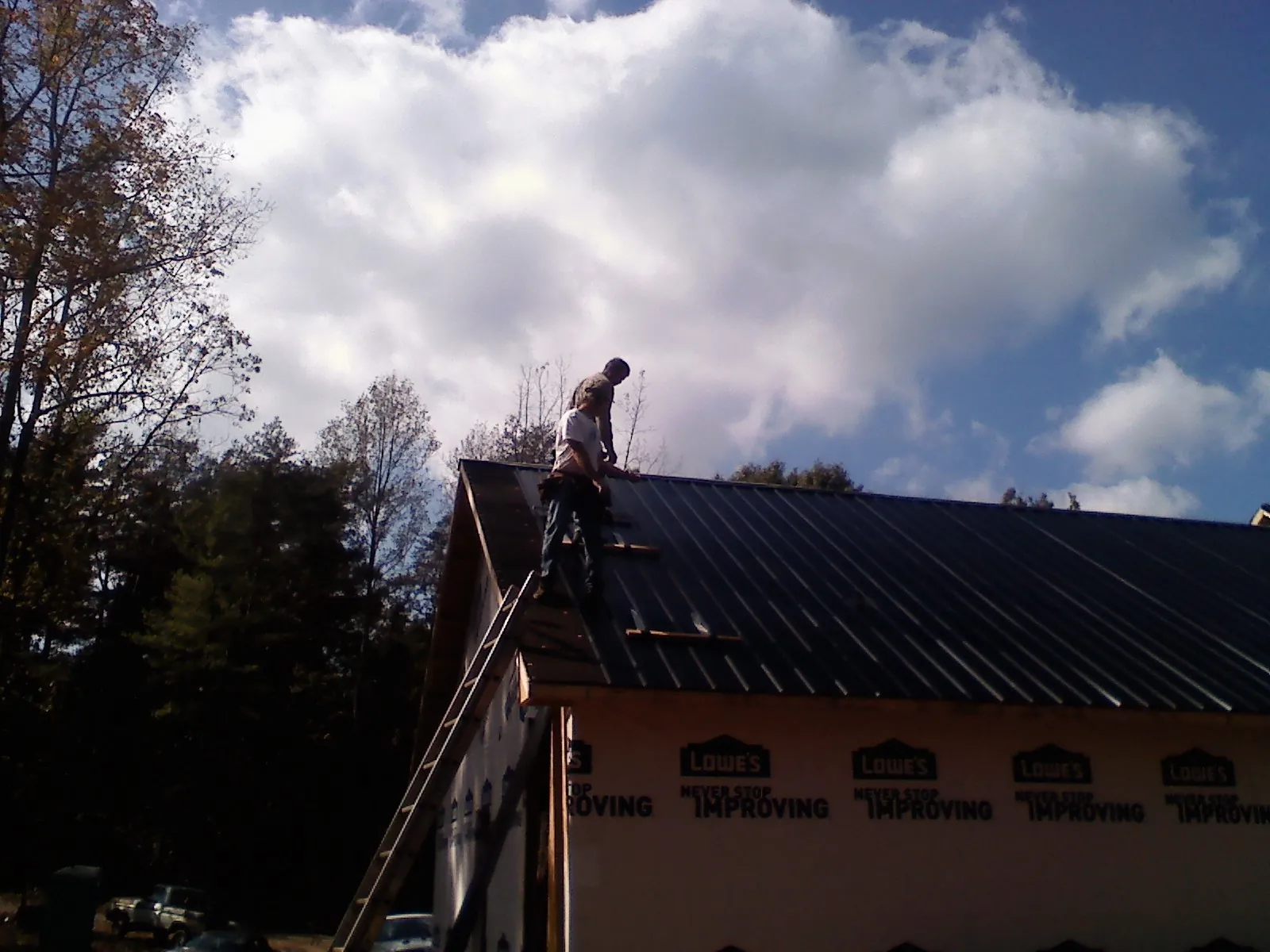Roofer fastening dark metal panels high against a cloudy sky, from a Roof Inspection job in Marshalltown