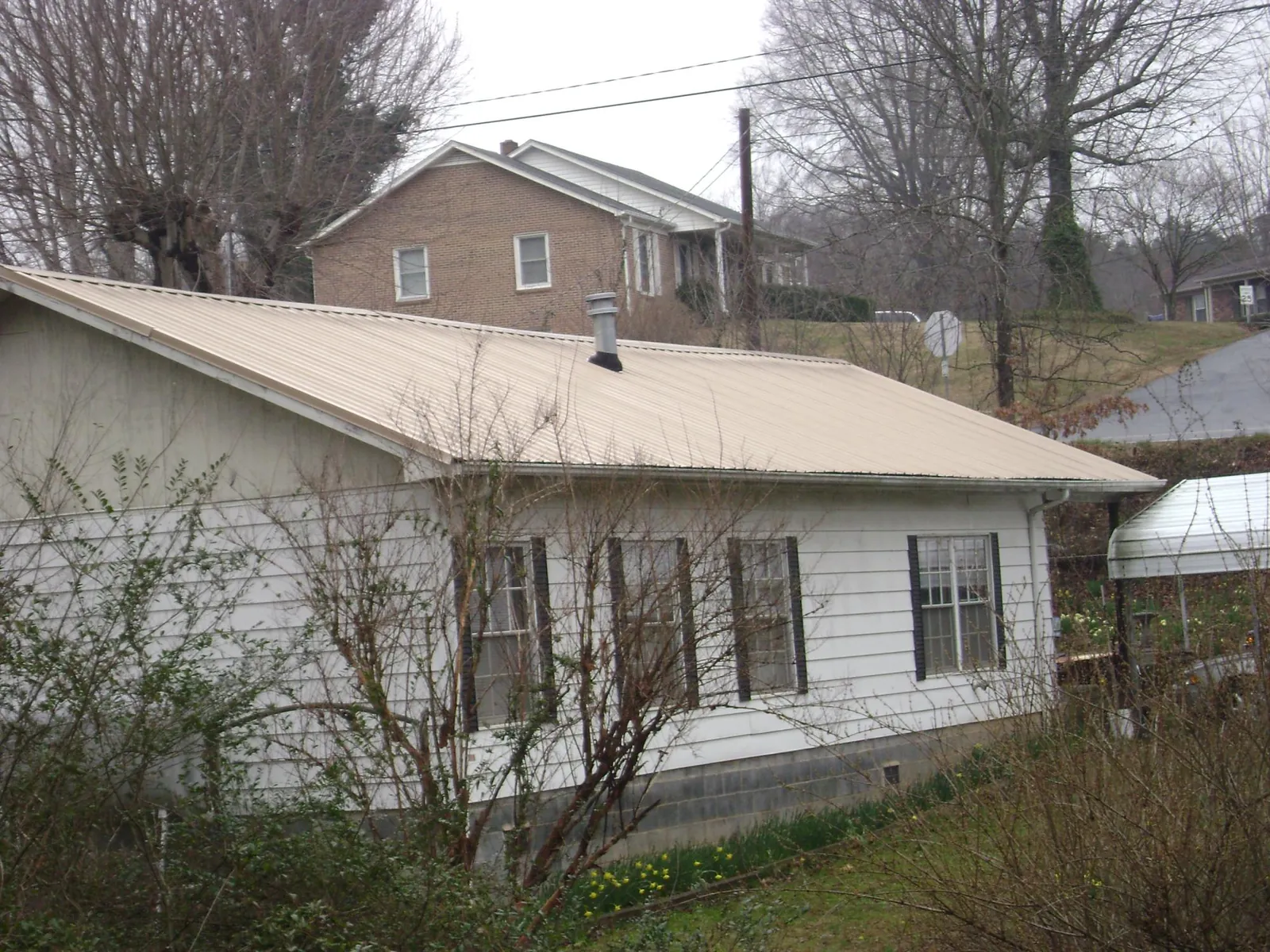 Tan metal roof on a white sided house set into a hillside — Commercial Roofing by Roofing Brothers in Marshalltown