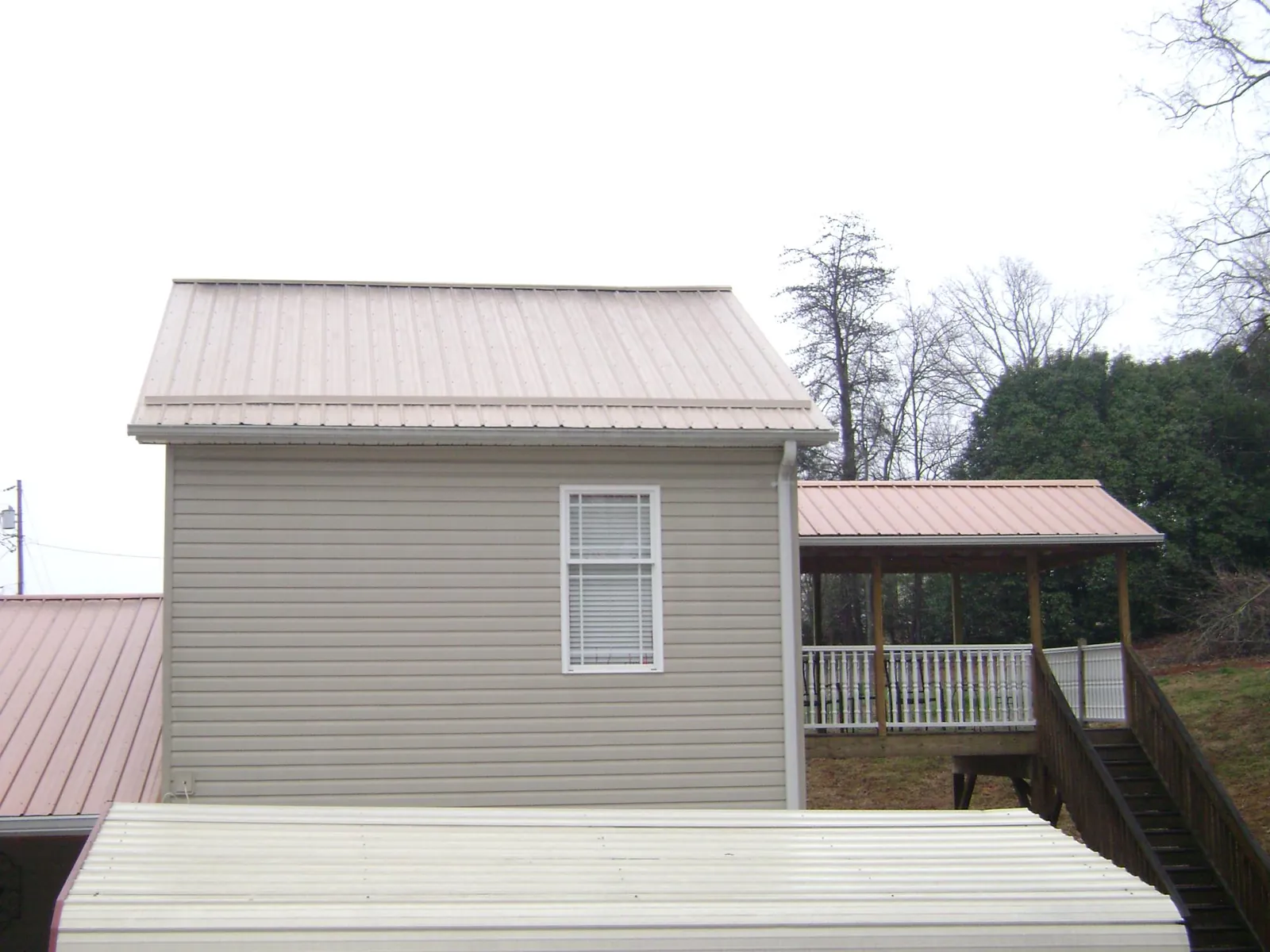 Tan metal roofs on a two story addition and attached porch, from a Roof Replacement job in Marshalltown