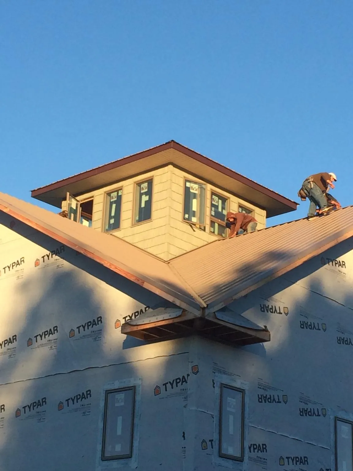Roofers working around a rooftop cupola on a new metal roof at sunset — Roof Waterproofing in Marshalltown by Roofing Brothers